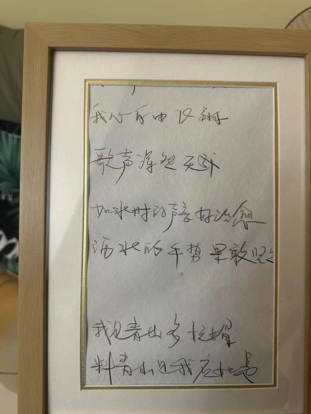 A framed page of handwritten Chinese lines in pencil, six lines in two groups.